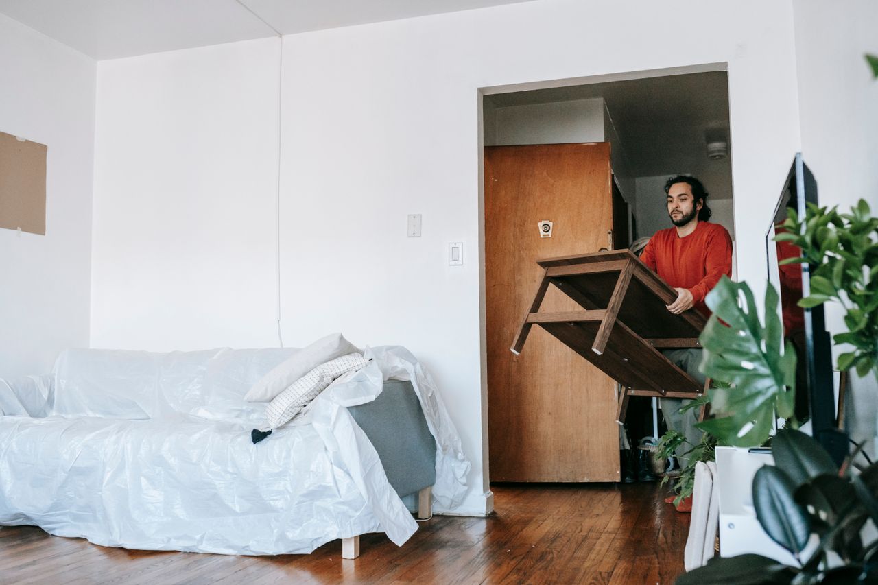 about-01 Man holding a wooden table during relocation in a contemporary apartment.